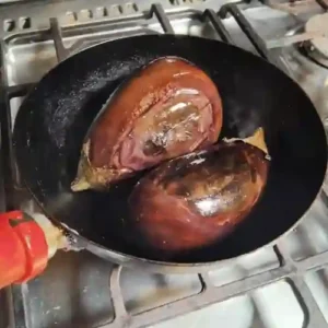 whole aubergine being sutéed in a cast iron wok