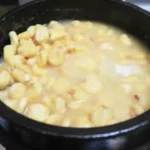 white corn being being nixtamalized in a lime wash solution in a black clay pot